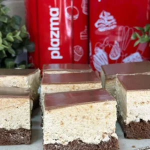 Narezane plazma kocke na tanjiru — čokoladni biskvit, kremasti sloj plazme i sjajna čokoladna glazura na vrhu, s plazma keksima u pozadini.