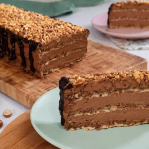 Kriška Dinastija torte na tanjuru s vidljivim slojevima čokoladne kreme i keksa, uz ostatak torte u pozadini na drvenoj dasci