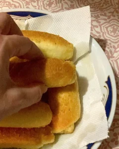 Ruka koja uzima posnu kiflu s tanjura obloženog papirom, prikaz zlatno pečenih kifli izbliza.