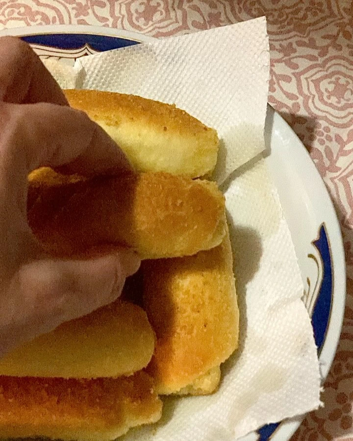 Ruka koja uzima posnu kiflu s tanjura obloženog papirom, prikaz zlatno pečenih kifli izbliza.