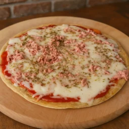 Cijela zdrava dijetalna pizza bez brašna s topljenim sirom, paradajz sosom i purećom salamom, fotografirana u toplom prirodnom svjetlu na drvenoj podlozi.