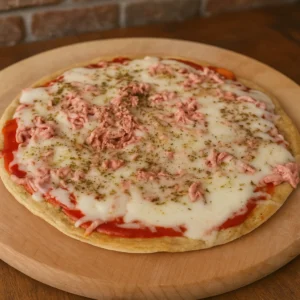 Cijela zdrava dijetalna pizza bez brašna s topljenim sirom, paradajz sosom i purećom salamom, fotografirana u toplom prirodnom svjetlu na drvenoj podlozi.