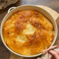 Zapečeni brzi burek sa sirom u okrugloj tepsiji, hrskave zlatne kore na drvenoj podlozi