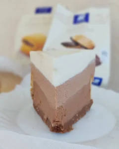 liski kadar vertikalnog komada cheesecakea koji prikazuje glatku teksturu slojeva i čokoladnu podlogu.