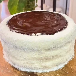Ruske kape torta premazana čokoladnim ganacheom i posuta kokosom, prikazana na drvenoj podlozi.