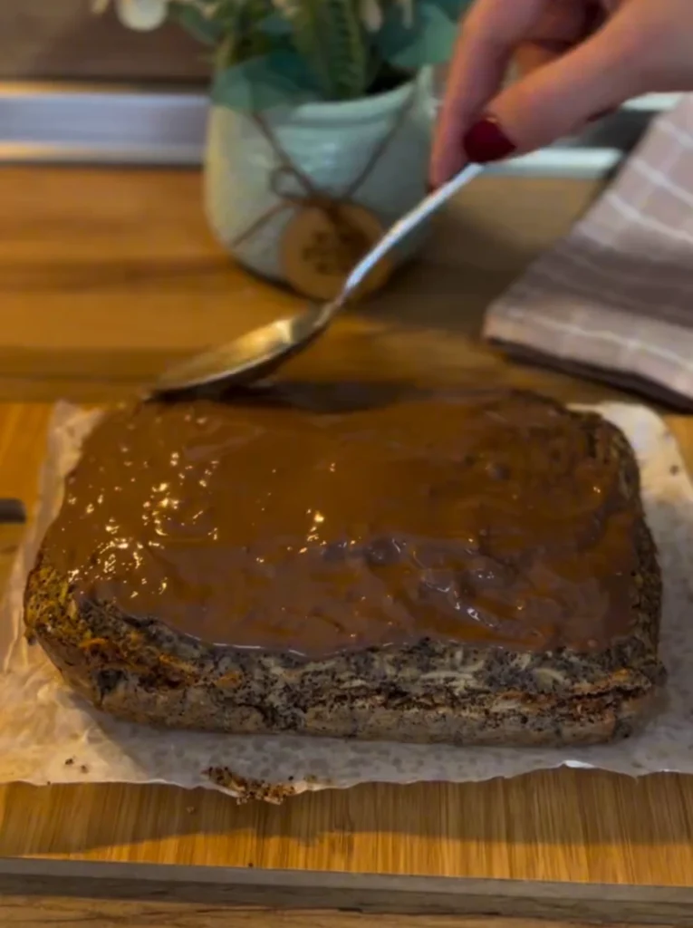 Razmazivanje otopljene čokolade preko pečenog kolača s makom