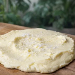 Domaći maslac od vrhnja za šlag s krupnom morskom soli na drvenoj dasci u toploj kuhinjskoj pozadini