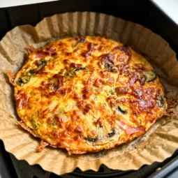 Pečeni airfryer omlet sa zlatnom koricom sira, šunkom i šampinjonima u košari airfryera