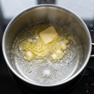 Kocka maslaca i prstohvat soli u loncu s vrelom vodom na indukcijskoj ploči, prvi korak pripreme choux tijesta