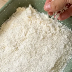 Ruka posipa ribani kokos i kokosove listiće preko sloja kreme u zelenom kalupu
