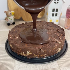Prelijevanje sjajne čokoladne glazure iz staklene posude preko torte s keksom i čokoladnim filom